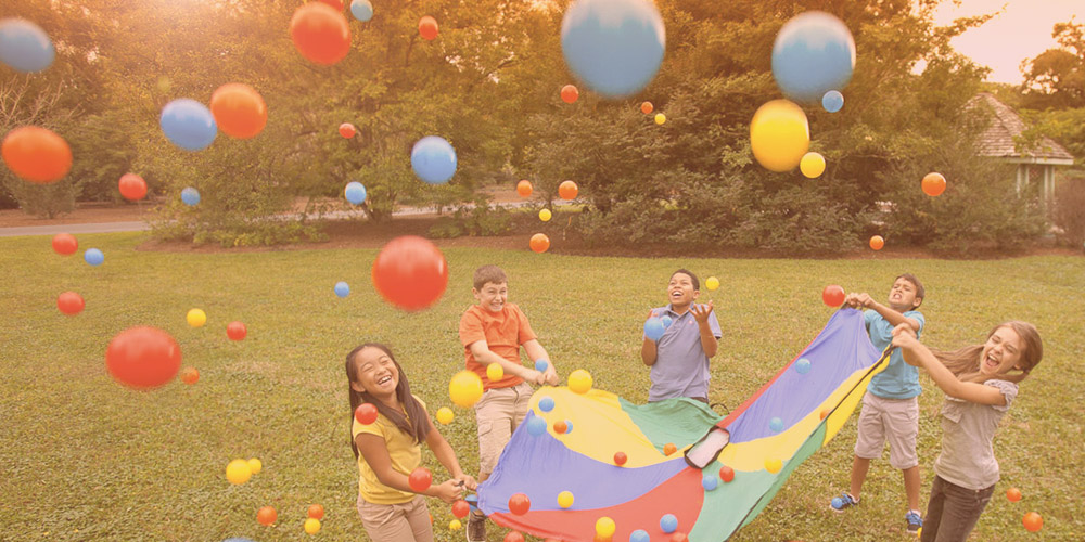 Children playing with a colorful parachute and balls